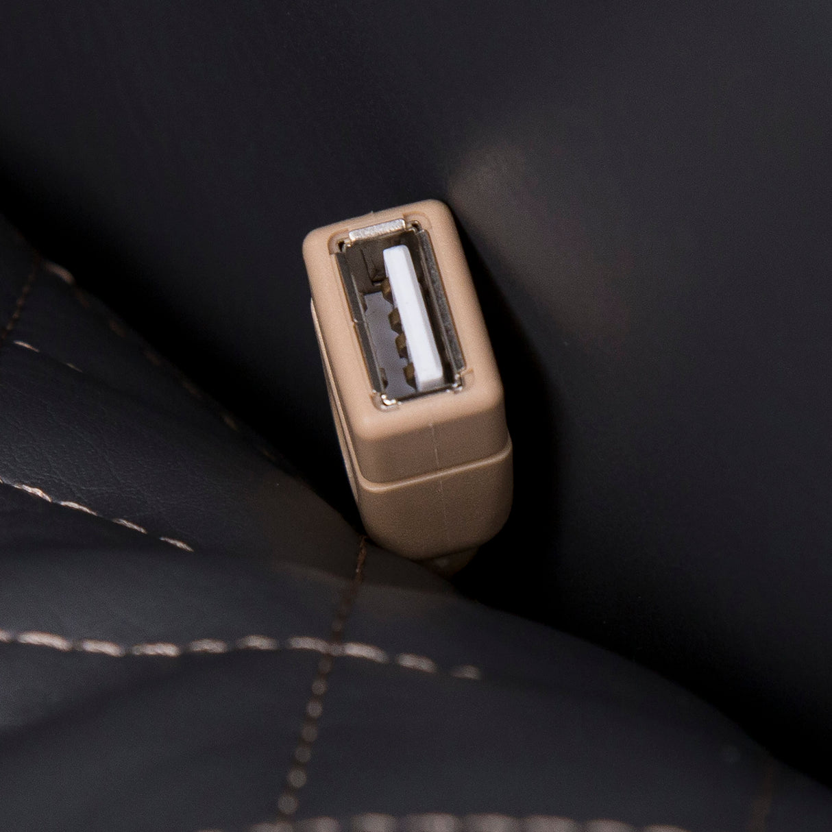 Close-up of USB port on the black leather surface of the Quies Massage Chair showing detailed stitching.