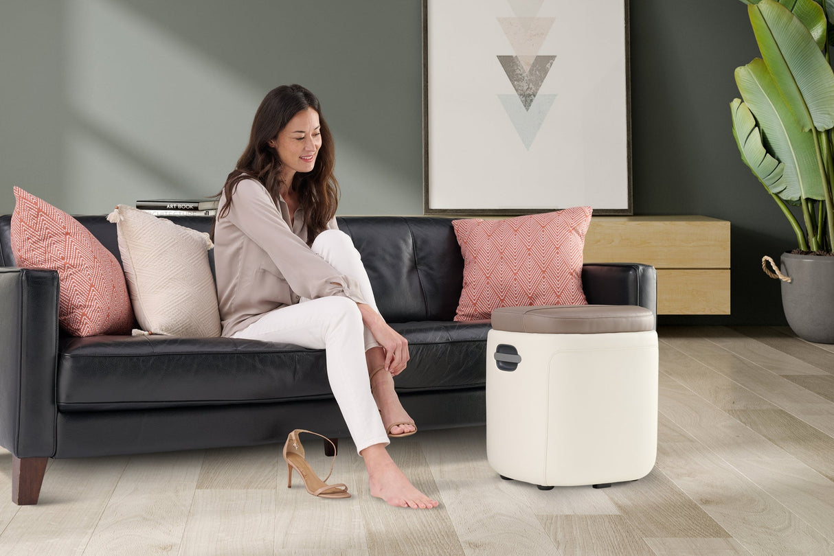 Reveal Ottoman Massager shown in modern living room with woman relaxing on couch using foot massage feature