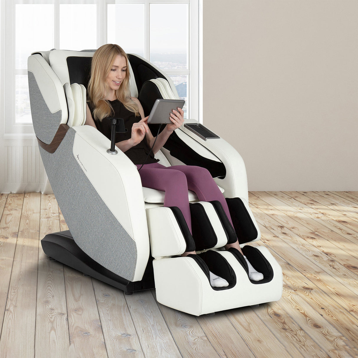 Woman relaxing in the WholeBody® ROVE Massage Chair using a tablet in a bright modern room.