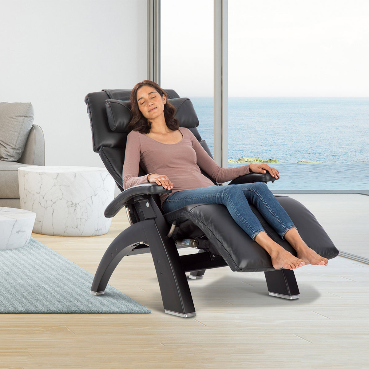 Perfect Chair PC-610 Omni-Motion Classic reclined in zero gravity position by ocean window, showcasing luxurious black leather design