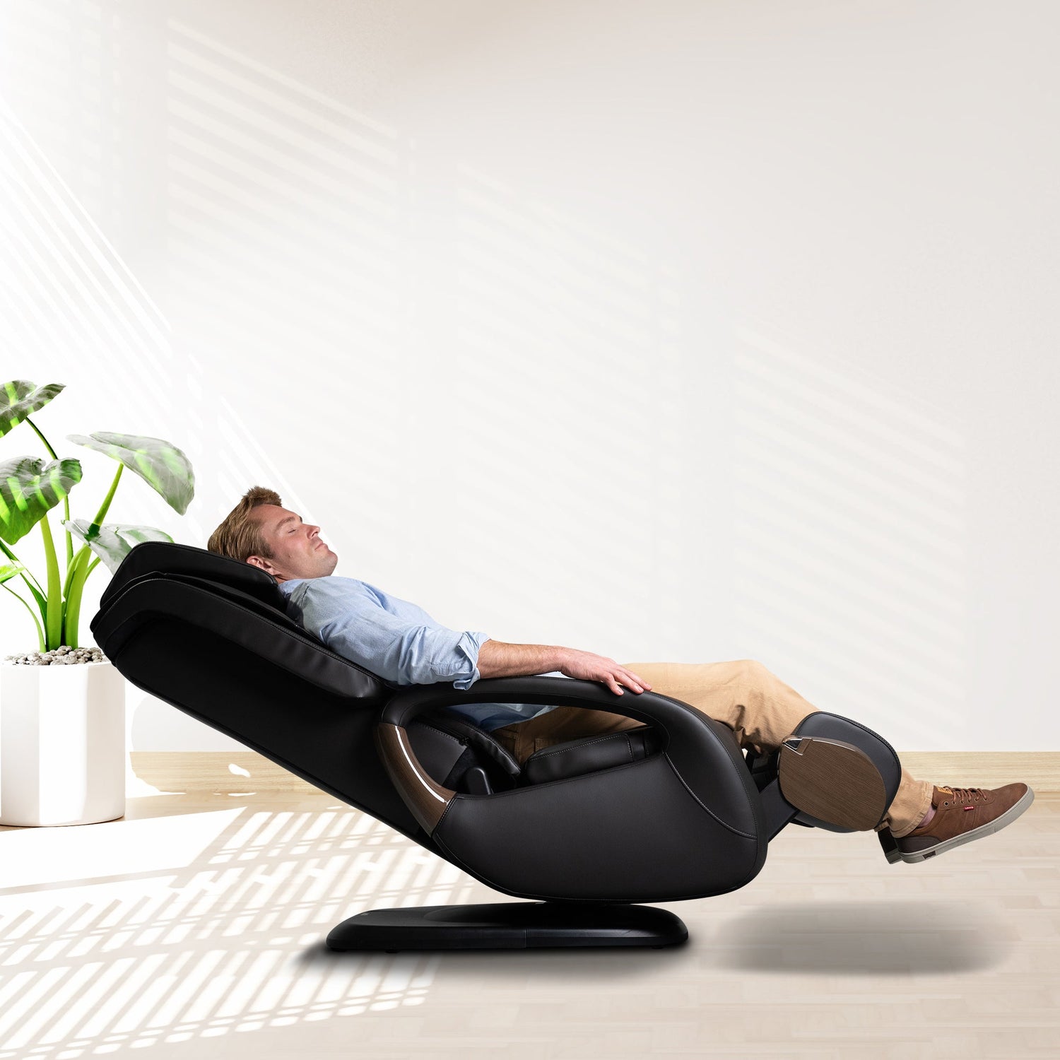 WholeBody 8.0 massage chair in black leather, fully reclined position in bright modern room with potted plant